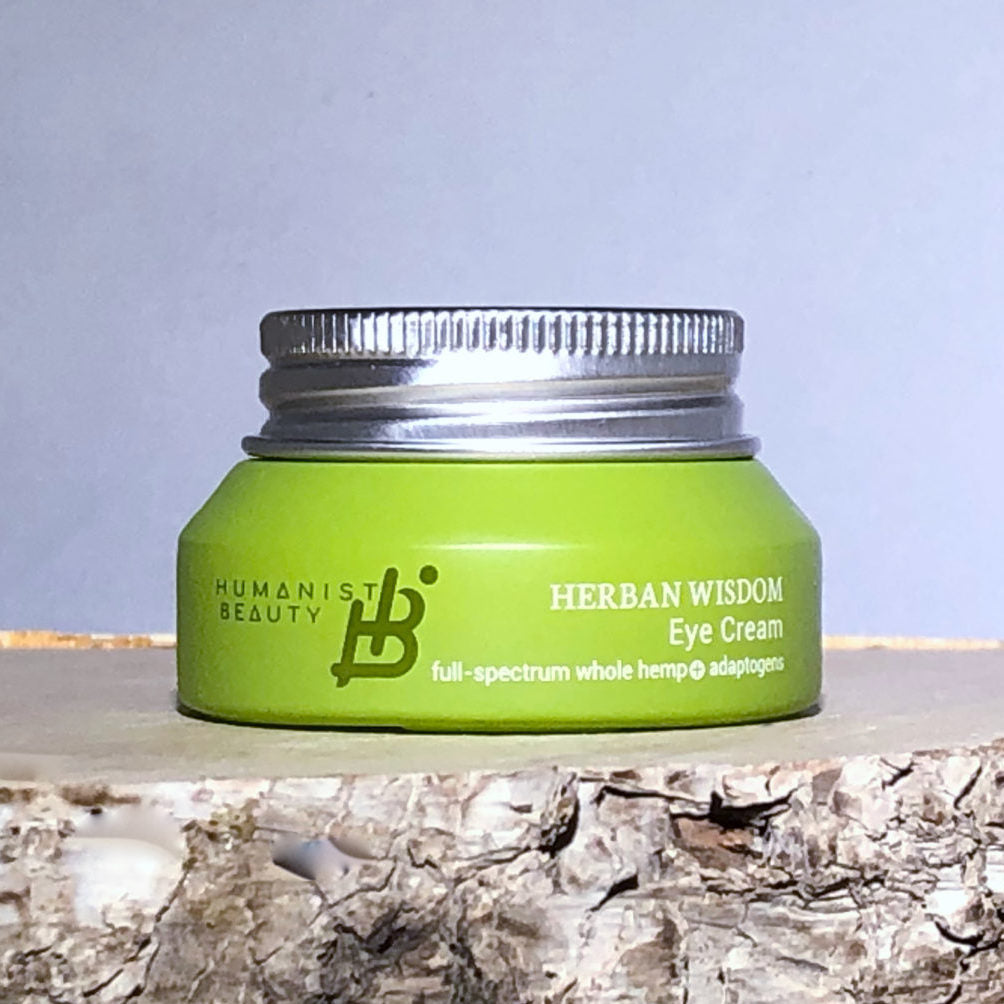 Green jar of Herban Wisdom Eye Cream on a wooden surface with a light blue background